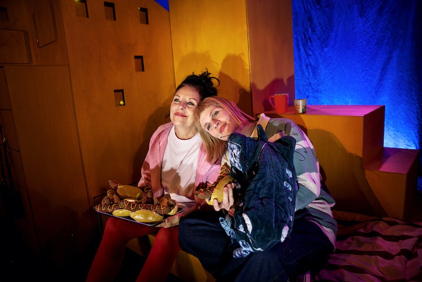 Foto Mamma och Åke som sitter i Åkes säng, ser glada ut och äter korv i bröd.